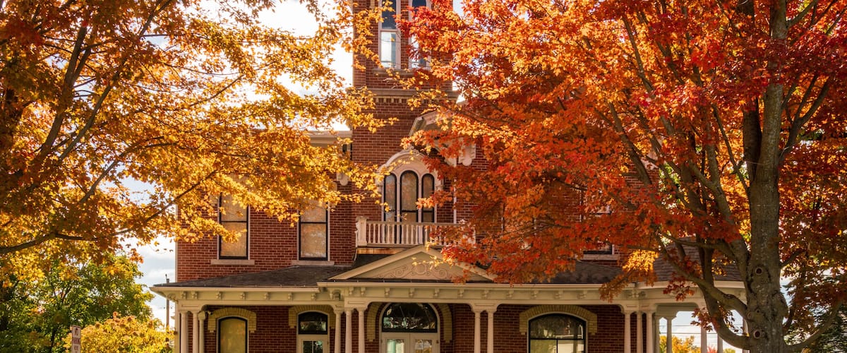 A Victorian-style house with a prominent tower, surrounded by autumn foliage.