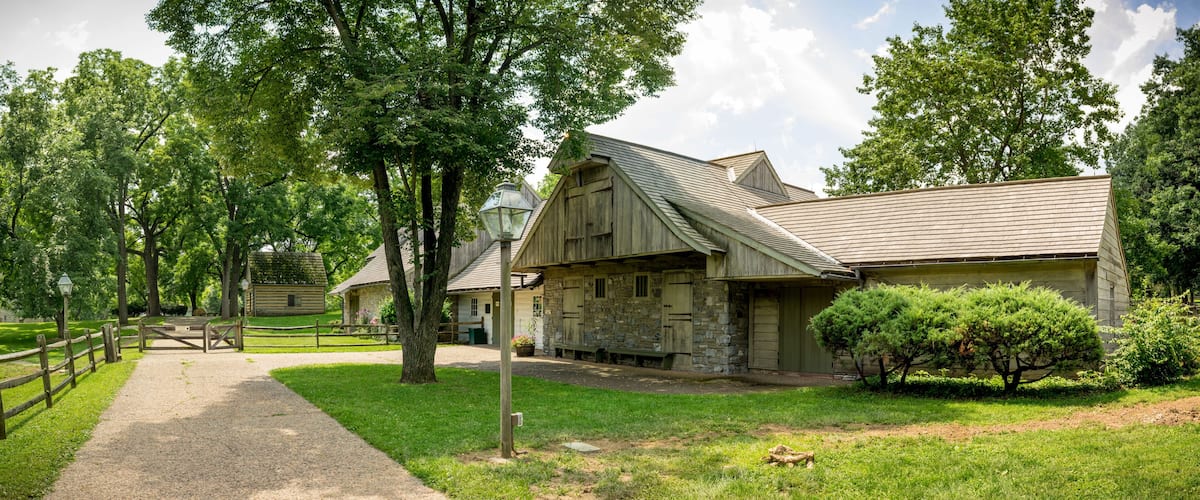 A rustic wooden building with a stone facade, surrounded by lush green trees and a gravel path.