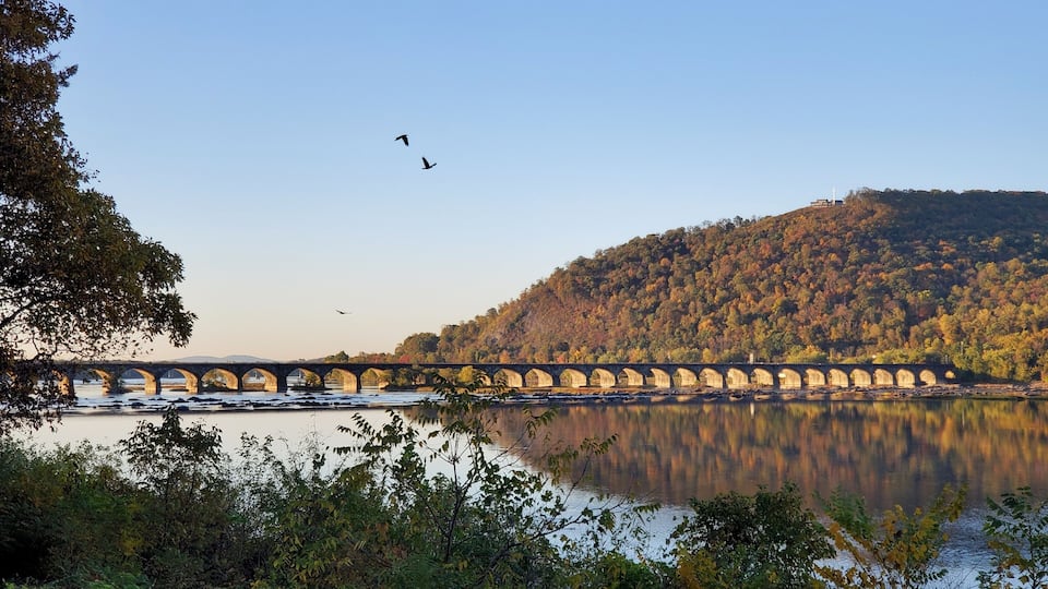 A stone bridge over a calm river with autumn foliage on the hills.