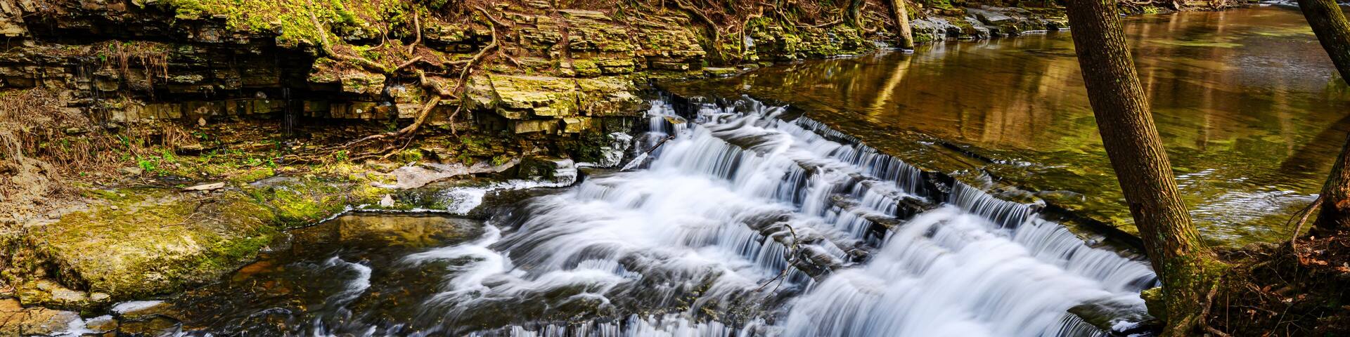 A partially frozen waterfall in late winter. Water rushes over and down the rocks at Salt Springs State Park in Montrose, PA. Heavy ice has already melted due to warmer temperatures.