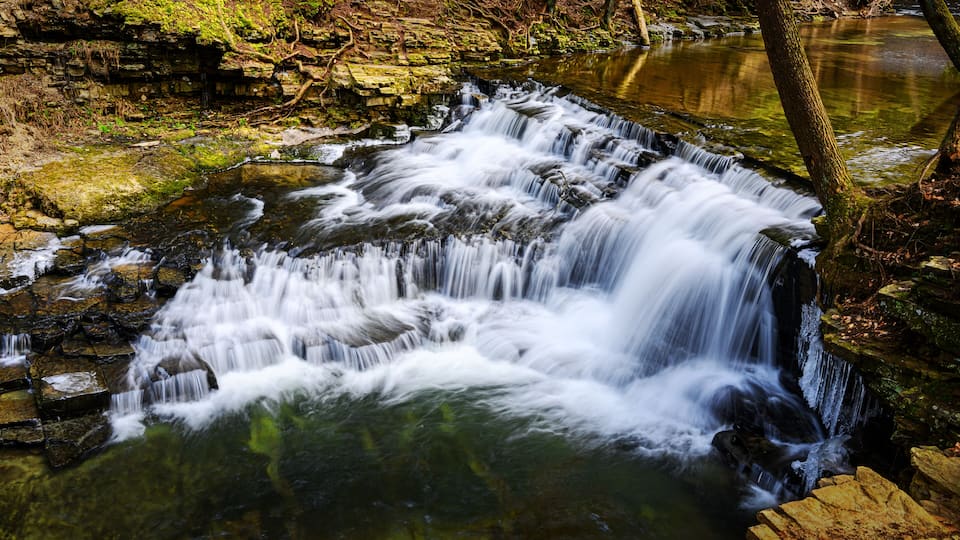 A multi-tiered waterfall cascading over rocks in a forested area.
