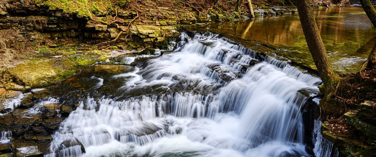 A multi-tiered waterfall cascading over rocks in a forested area.