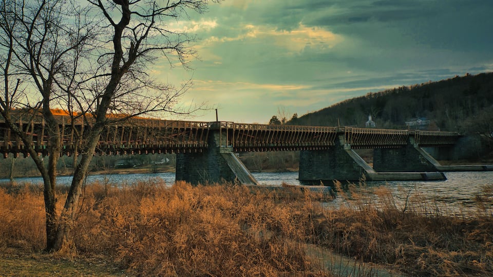 A bridge over a river with a forested hillside in the background.