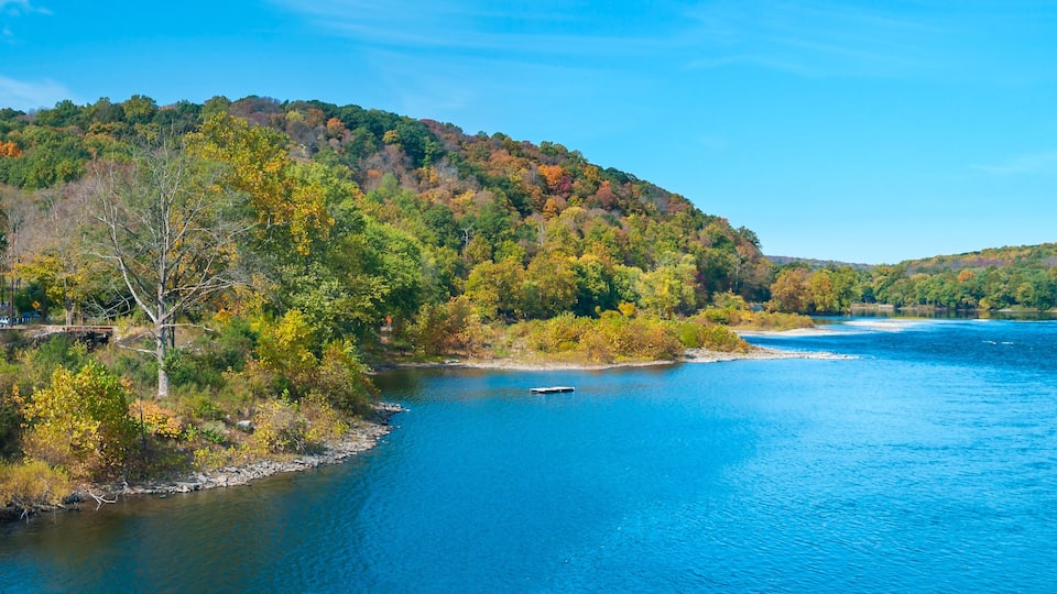 A river surrounded by autumn-colored trees and a clear blue sky.