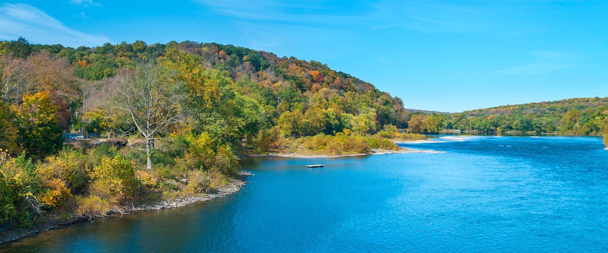 A river surrounded by autumn-colored trees and a clear blue sky.