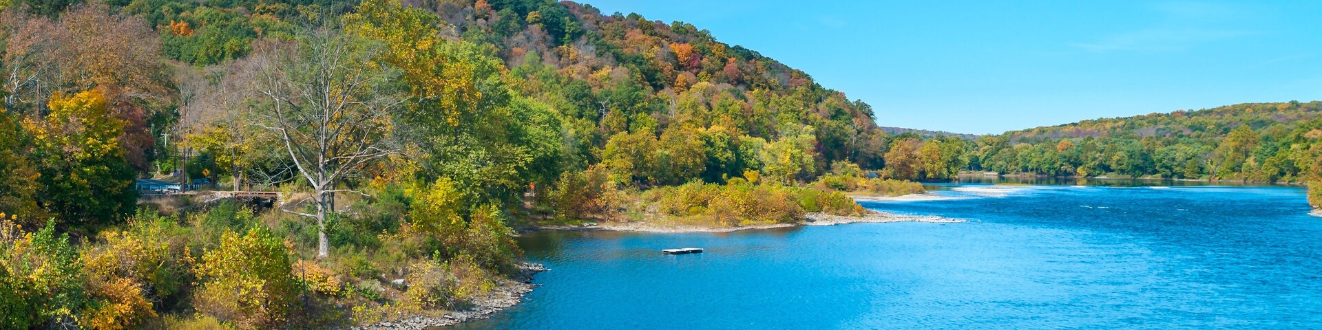 A river surrounded by autumn-colored trees and a clear blue sky.