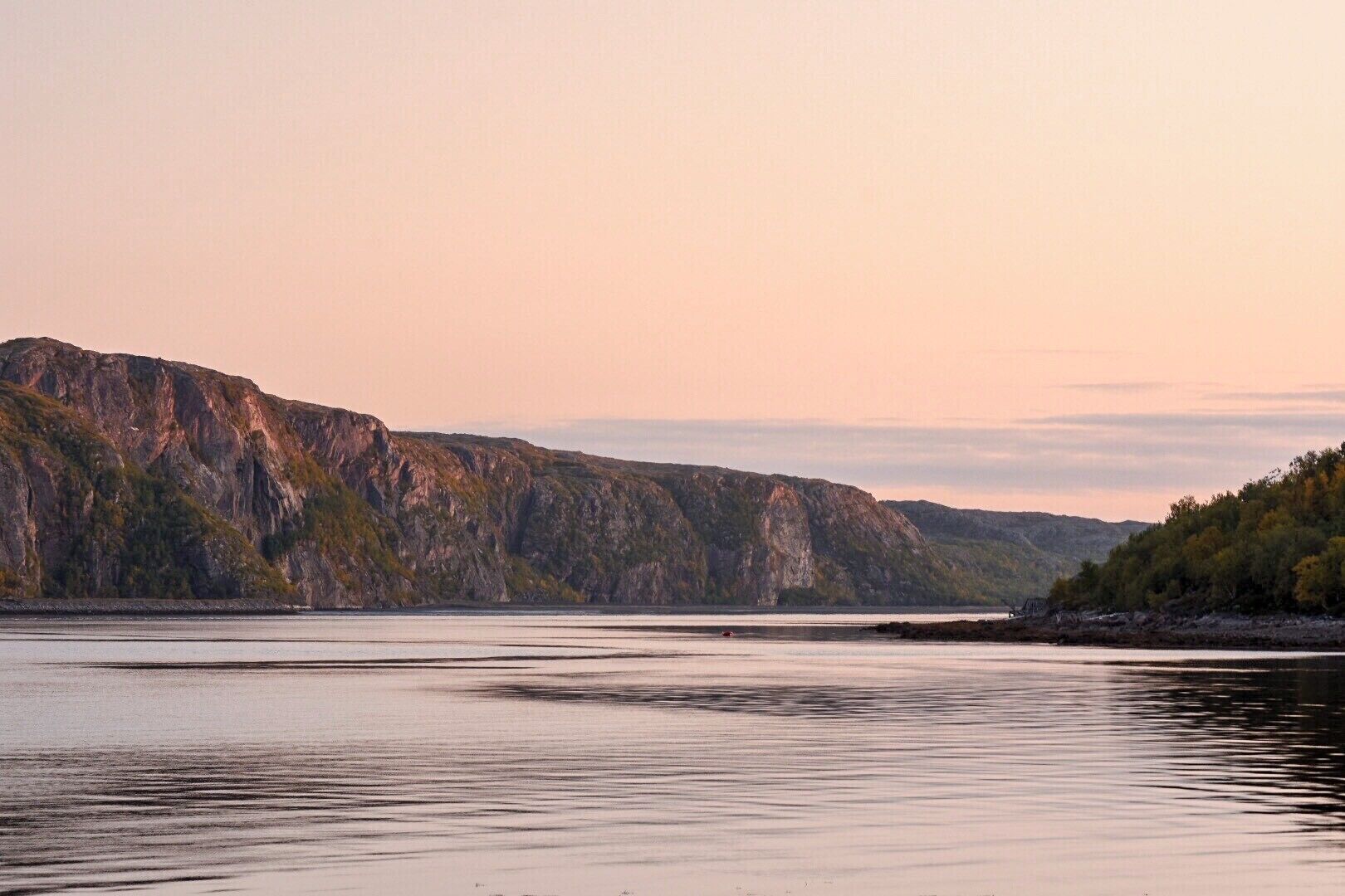 A calm river with rocky cliffs and trees in the background.