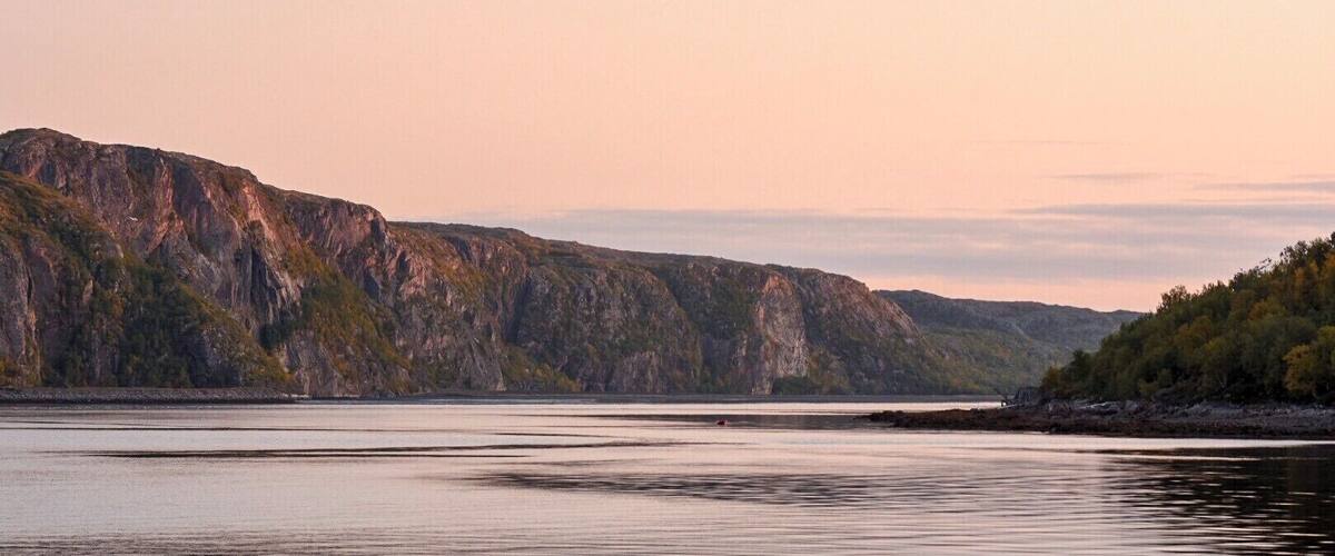A calm river with rocky cliffs and trees in the background.