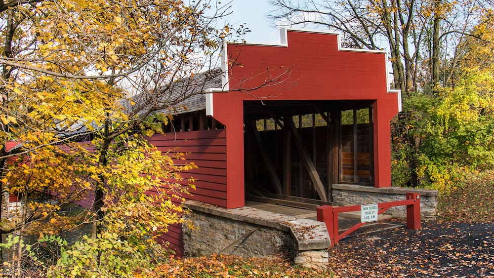 A red wooden structure with a stone base, surrounded by autumn foliage.