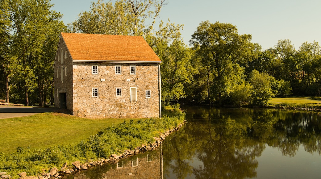 Landscape of an old stone house next to a winding river surrounded by summer trees and grass