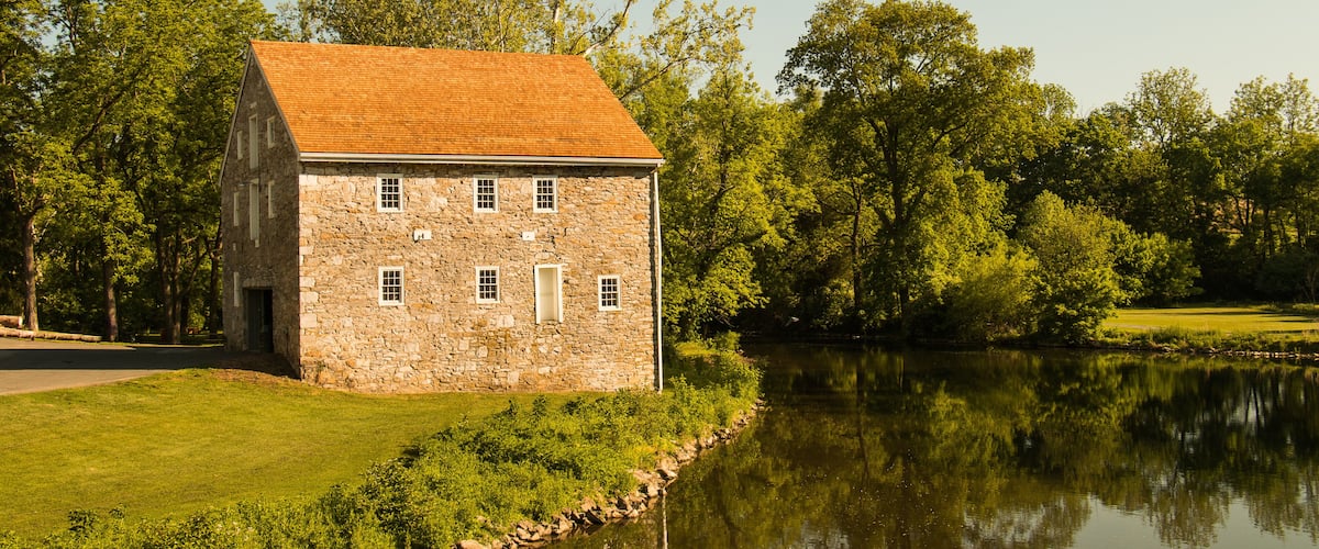Landscape of an old stone house next to a winding river surrounded by summer trees and grass