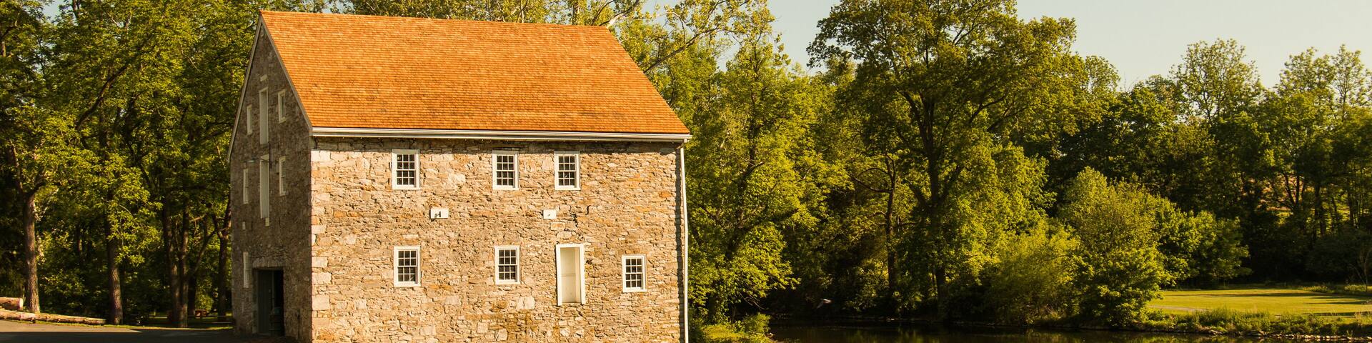 Landscape of an old stone house next to a winding river surrounded by summer trees and grass