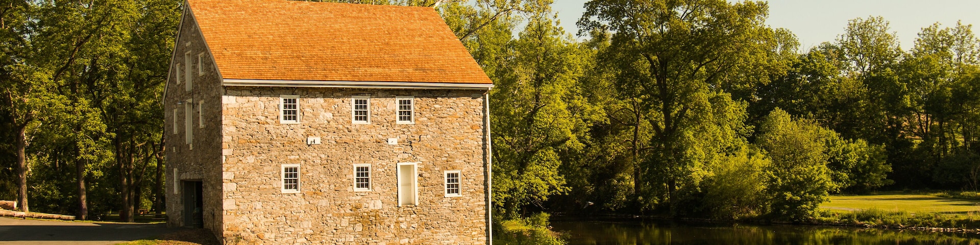 Landscape of an old stone house next to a winding river surrounded by summer trees and grass