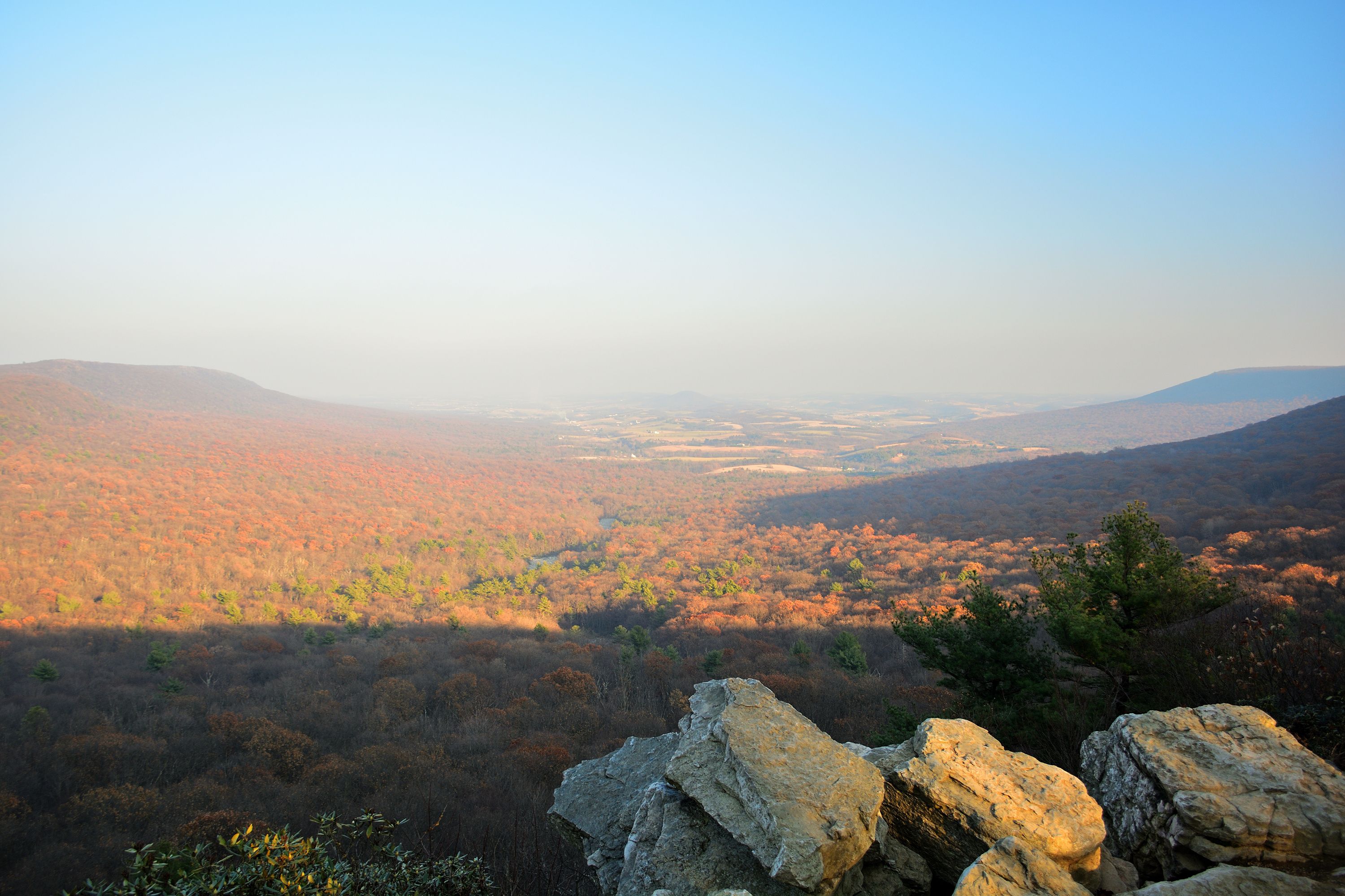 A mountainous landscape with autumn foliage, rocky outcrops, and a valley below.
