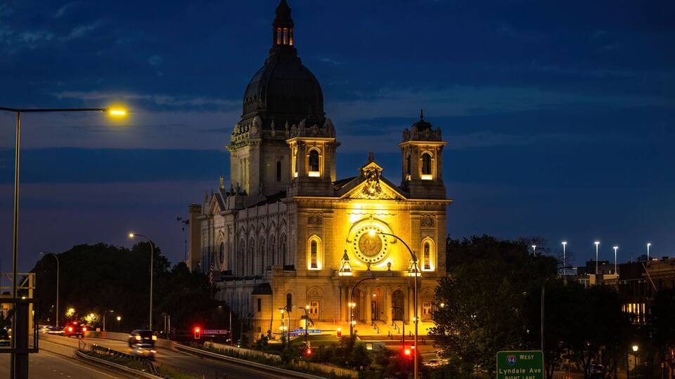 A large cathedral with a prominent dome and clock, situated beside a highway.