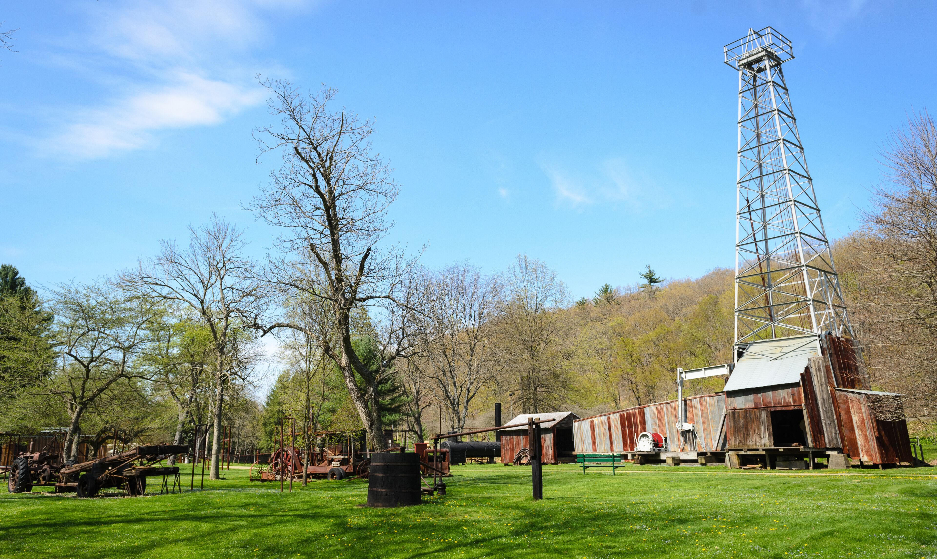 A rural landscape with a tall metal tower, a rusted barn, and vintage farming equipment.