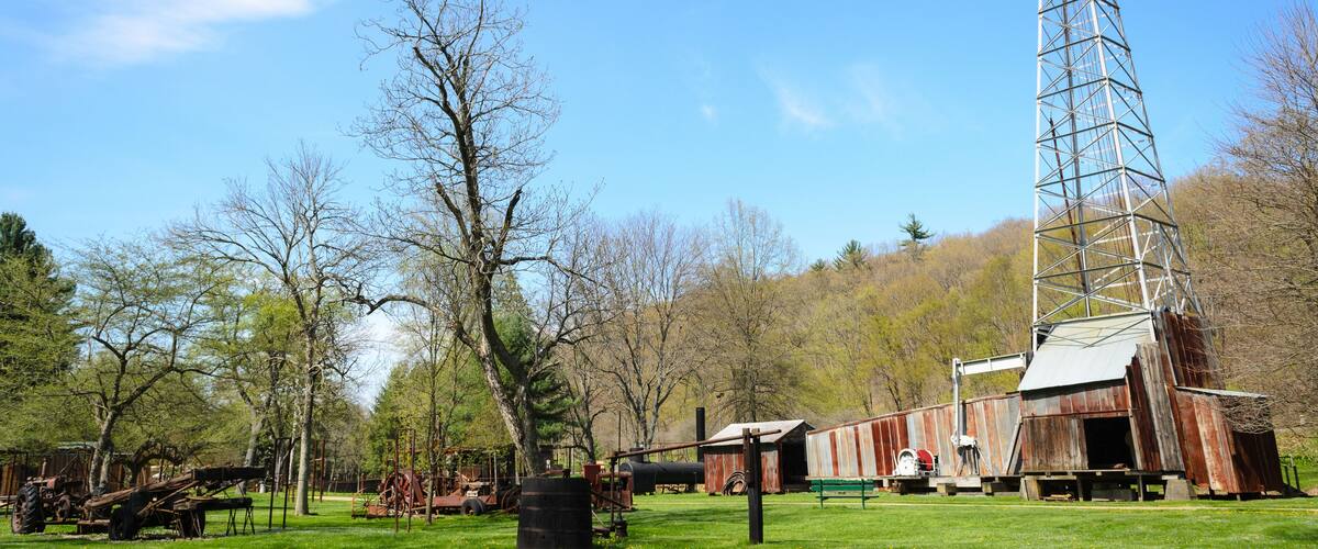 A rural landscape with a tall metal tower, a rusted barn, and vintage farming equipment.