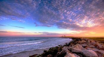 A coastal landscape with a rocky shoreline, waves, and a distant lighthouse.