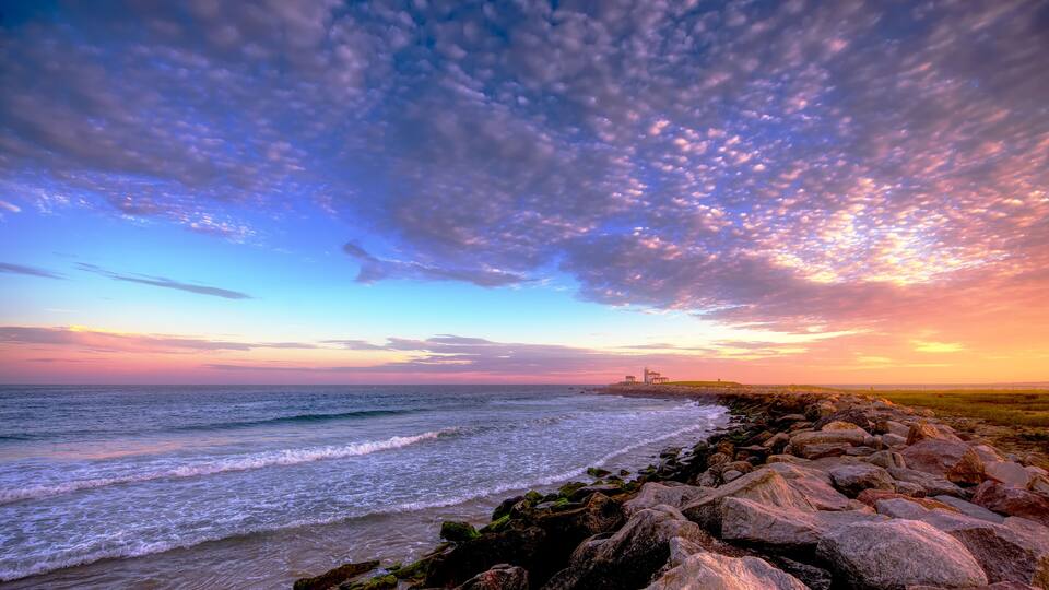 A coastal landscape with a rocky shoreline, waves, and a distant lighthouse.