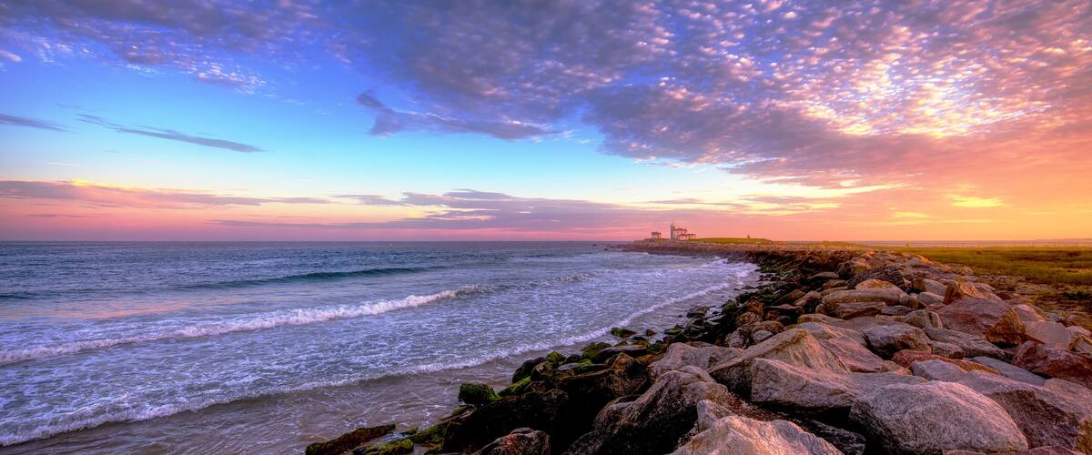 A coastal landscape with a rocky shoreline, waves, and a distant lighthouse.