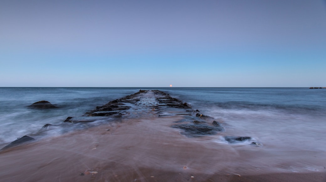 Eine lange Mole, die sich in ruhiges Wasser erstreckt, mit blauem Himmel.