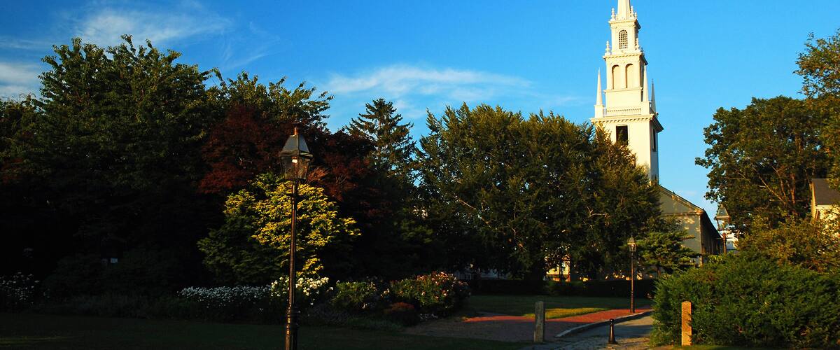 A church with a tall steeple, surrounded by trees and a pathway.