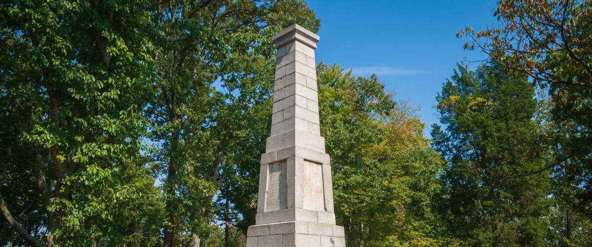A stone monument with a stepped base surrounded by trees.