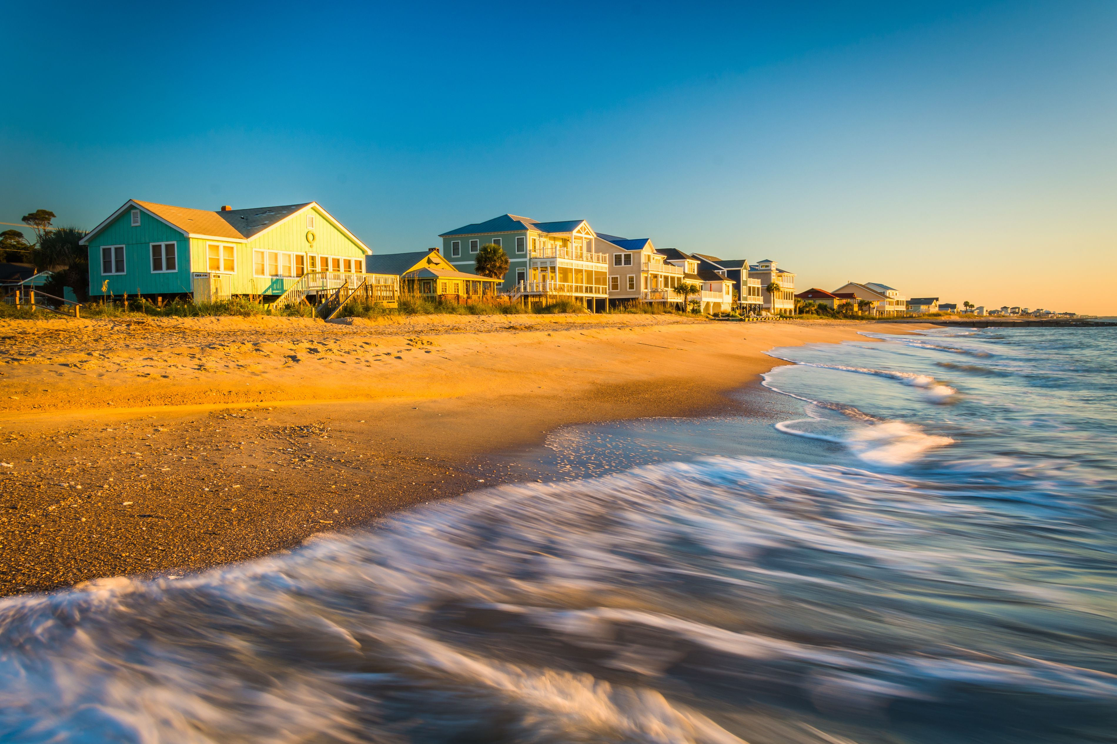 A beach with houses along the shore and waves crashing onto the sand.