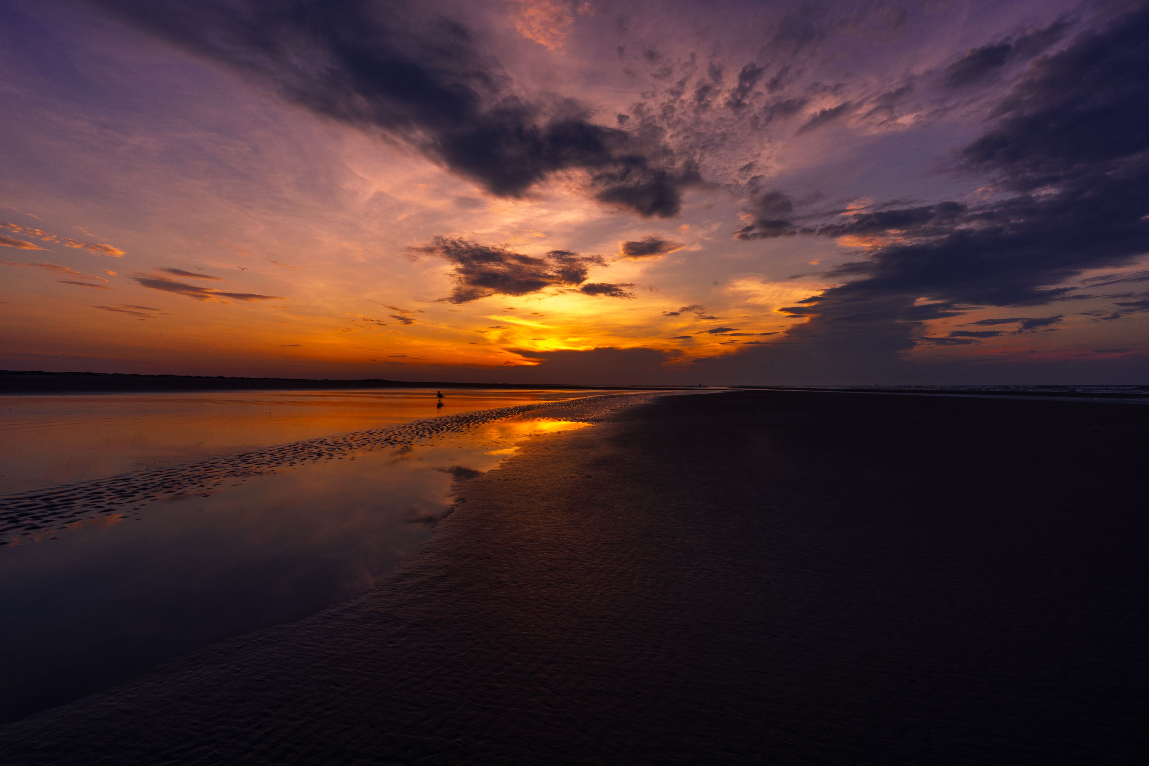 Un coucher de soleil sur une plage paisible, avec une personne qui se promène le long du rivage.