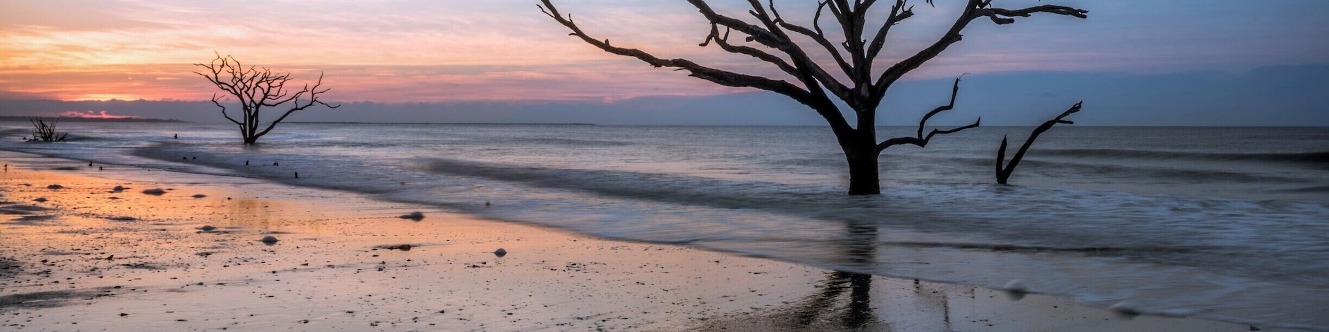 A very early morning outing at Botany Bay on Edisto Island. I had to start from my hotel at 3 AM to make it to this location before dawn. 
Botany Bay Plantation is a nature preserve and has regulated visitor hours. Gates open 30 minutes before sunrise - I wish they'd open a little sooner as the golden hour is pretty much more than half way done by the time one can make it to the beach. Nevertheless, it's a great location to visit at sunrise, especially if there are high clouds to add drama. Recommended to visit when the tide is ebbing as you then get the shadows of the trees, which to my eyes add more depth to the image. 
On this day, there was a bank of low clouds that prevented too much color but it was a great sunrise to witness nonetheless. The trees have so much character and add so much to the image. It's hard to look at the remnants of these trees and not imagine the onslaught they've withstood at the hands of mother nature. 
#WeekendGetAwayForTheFamily #colorful #USA #weekend #treetrove #blue