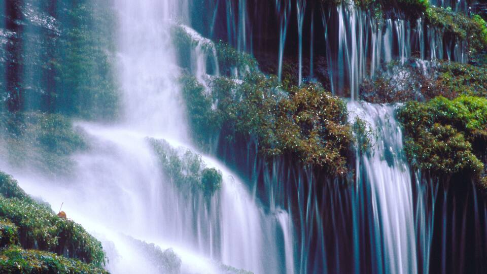 A multi-tiered waterfall surrounded by lush greenery.