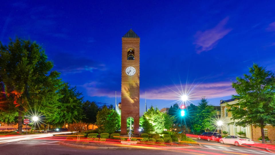 A tall brick clock tower with a clock face, surrounded by trees and streetlights.