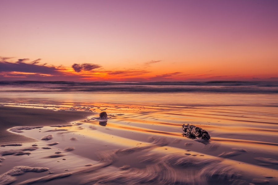 A beach at sunset with a calm sea, a rock formation, and footprints in the sand.