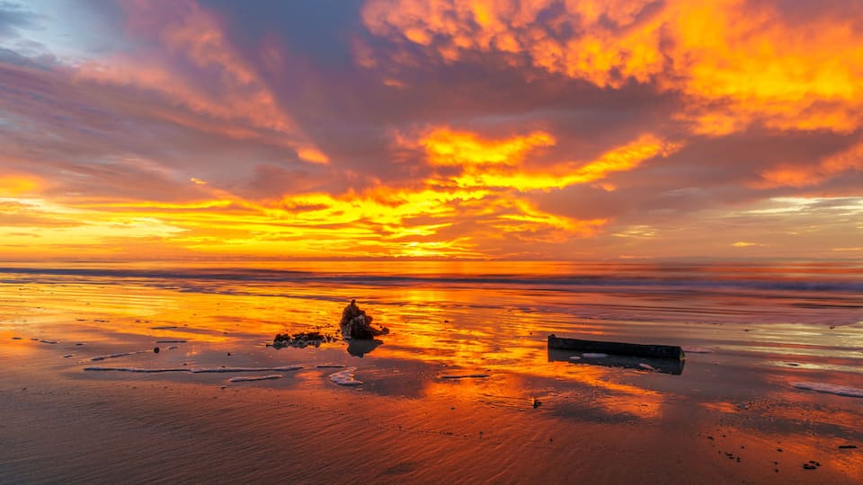 A sunset over a beach with a large rock formation and a wooden structure.