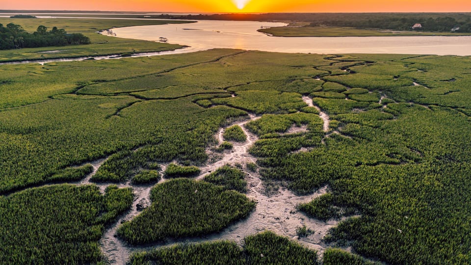 A river meandering through a lush green landscape with a sunset in the background.