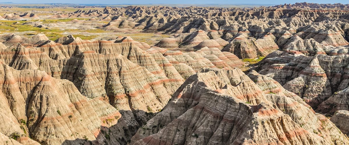 A vast landscape of rugged, colorful badlands with distinct erosion patterns and sparse vegetation.
