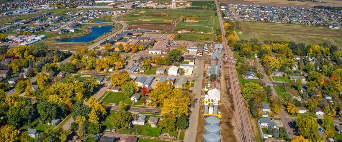An aerial view of a town with a large industrial area, a sports field, and surrounding residential neighborhoods.