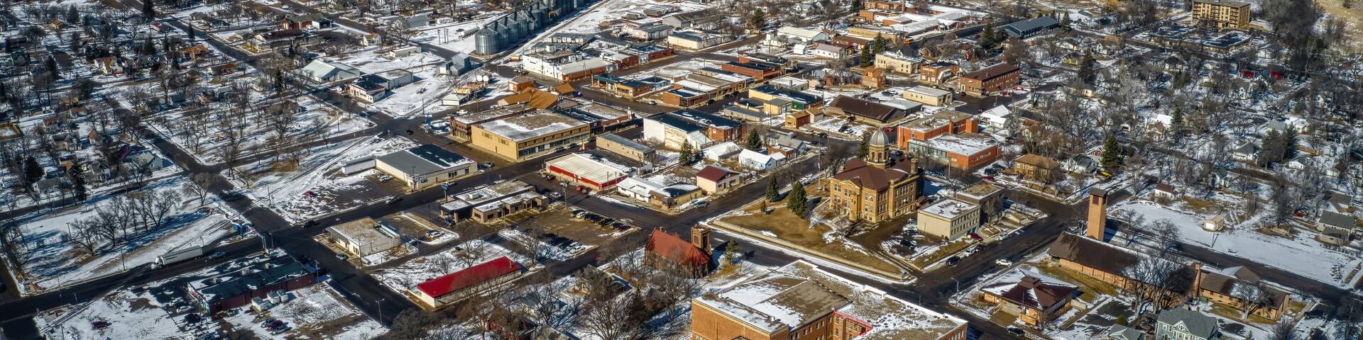 An aerial view of a snow-covered town with distinct buildings, roads, and surrounding fields.