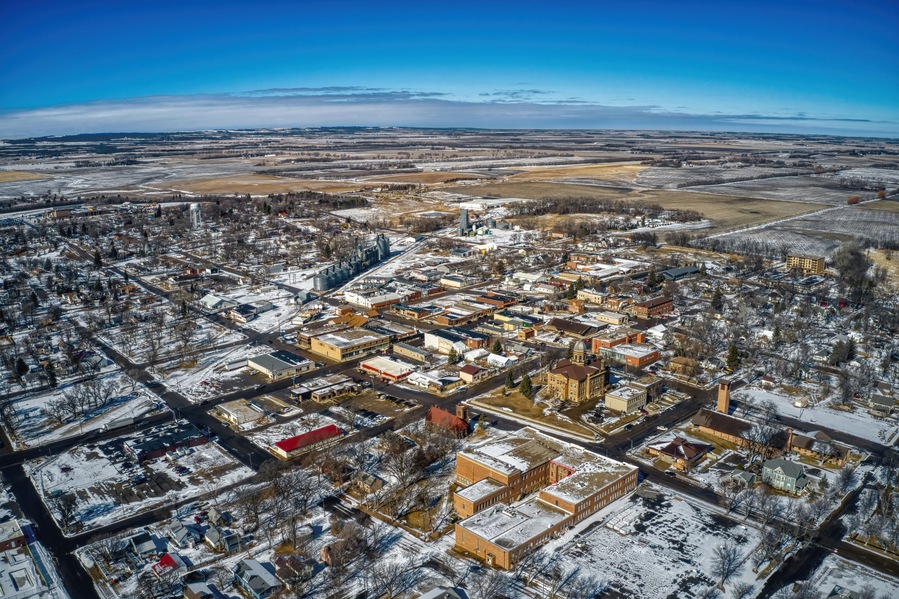 An aerial view of a snow-covered town with distinct buildings, roads, and surrounding fields.