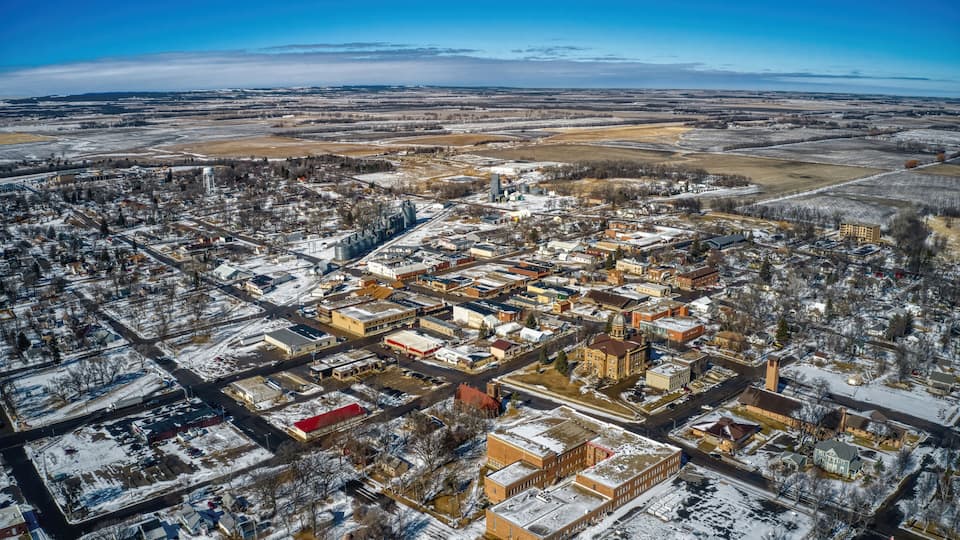 An aerial view of a snow-covered town with distinct buildings, roads, and surrounding fields.