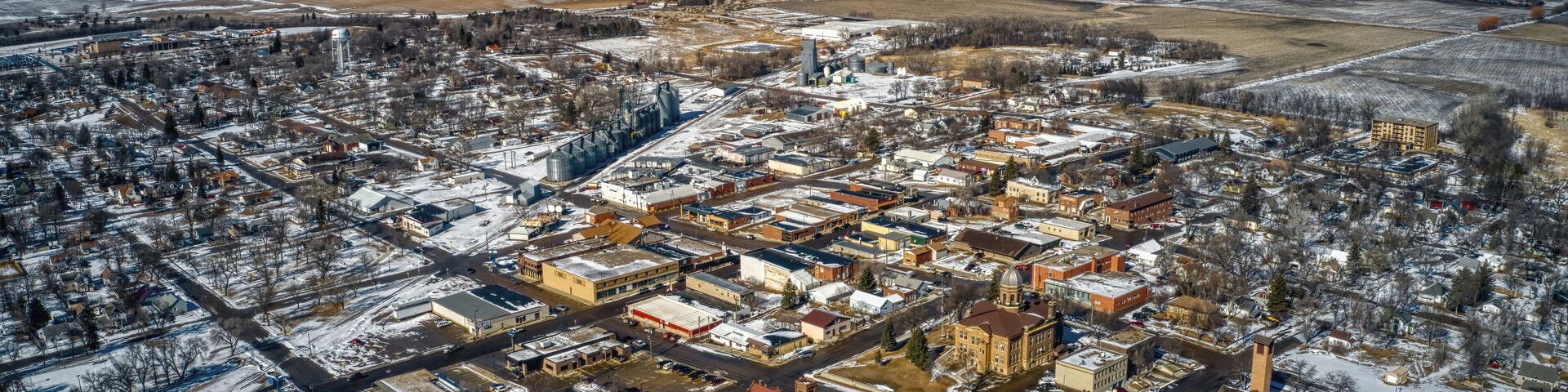 An aerial view of a snow-covered town with distinct buildings, roads, and surrounding fields.