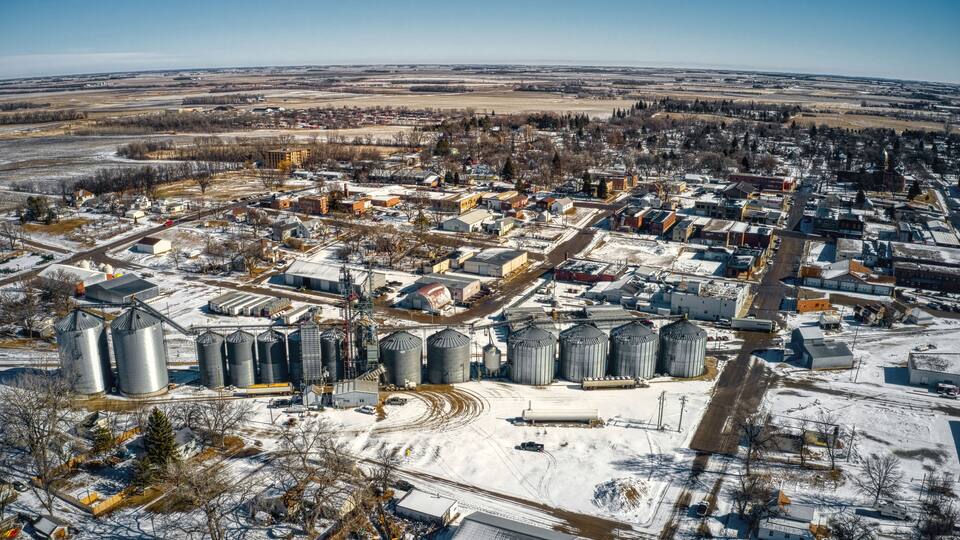 An industrial area with multiple grain silos and storage buildings, surrounded by a small town with residential houses and roads.