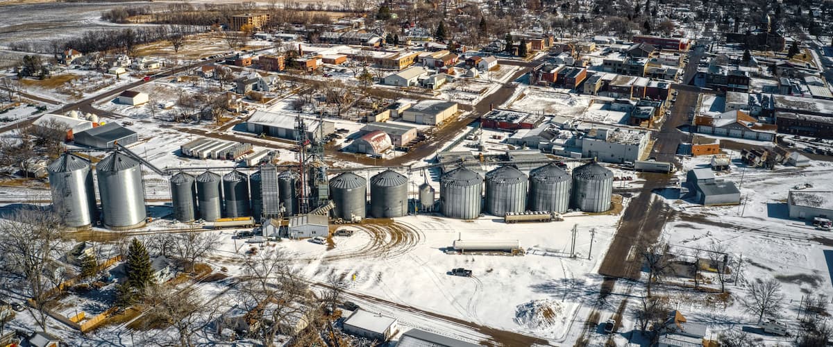 An industrial area with multiple grain silos and storage buildings, surrounded by a small town with residential houses and roads.