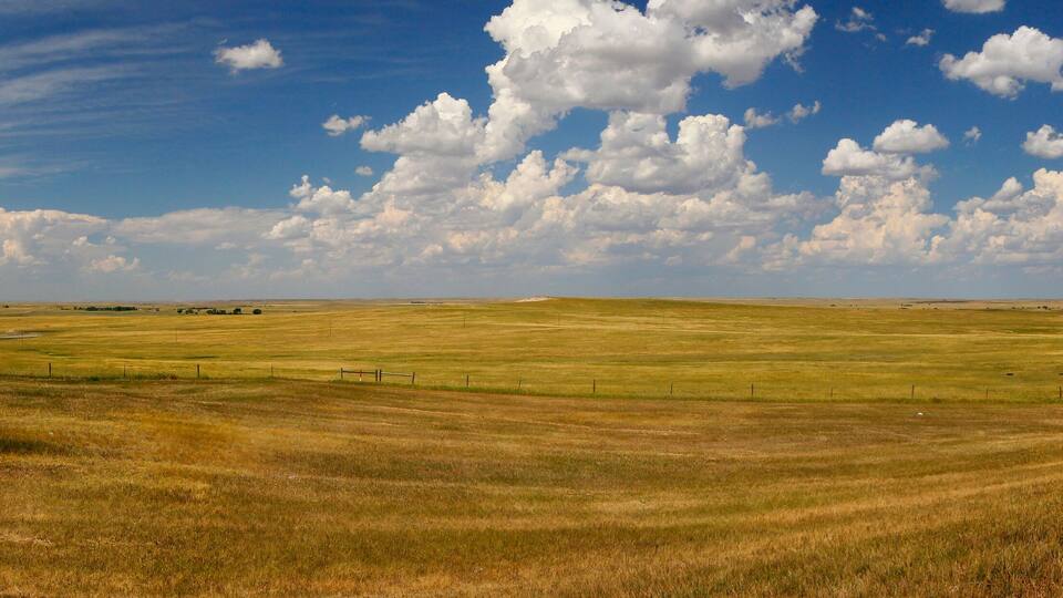 A vast open field with rolling hills under a partly cloudy sky.
