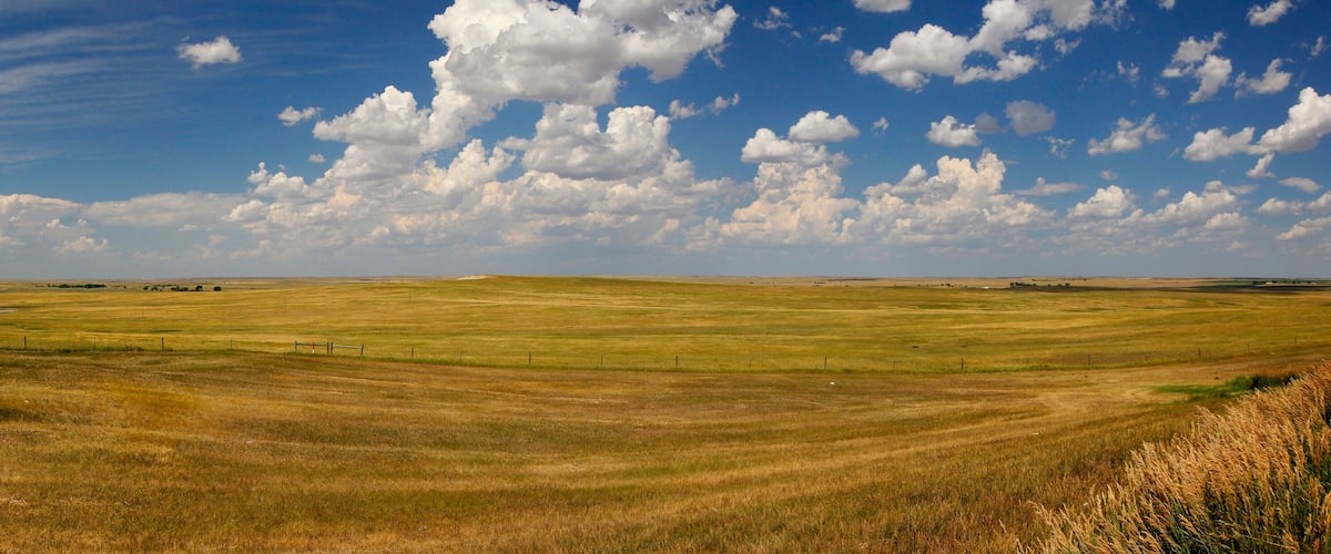 A vast open field with rolling hills under a partly cloudy sky.
