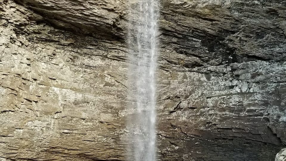 A waterfall cascading down a rocky cliff into a calm pool surrounded by bare trees.