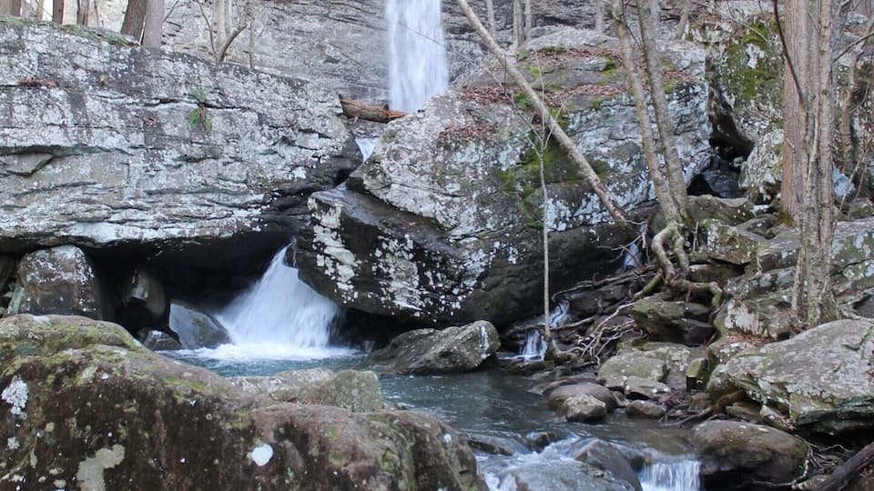 A waterfall in a forested area with large rocks and trees.