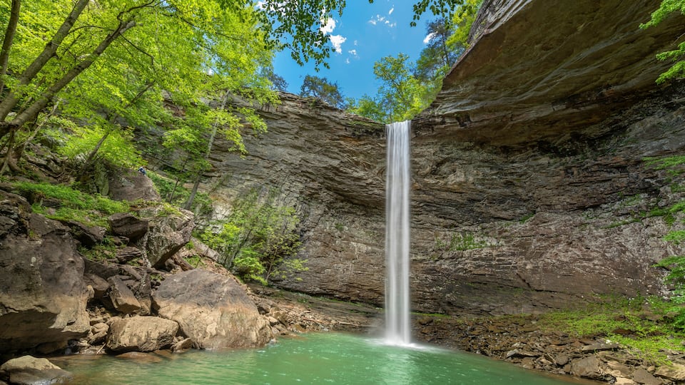 A waterfall cascading into a clear green pool surrounded by rocky cliffs and lush green trees.