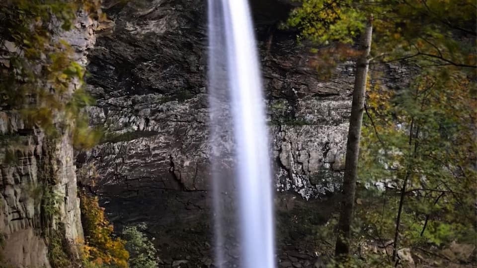A waterfall cascading down a rocky cliff surrounded by autumn foliage.