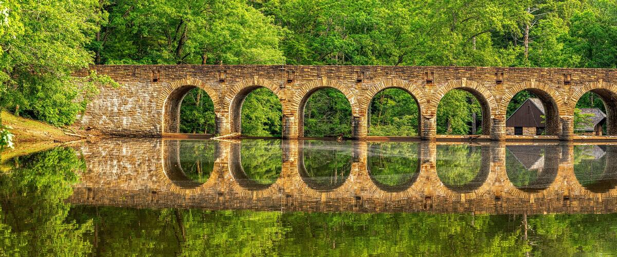 A stone bridge with multiple arches over a calm river, surrounded by lush greenery.